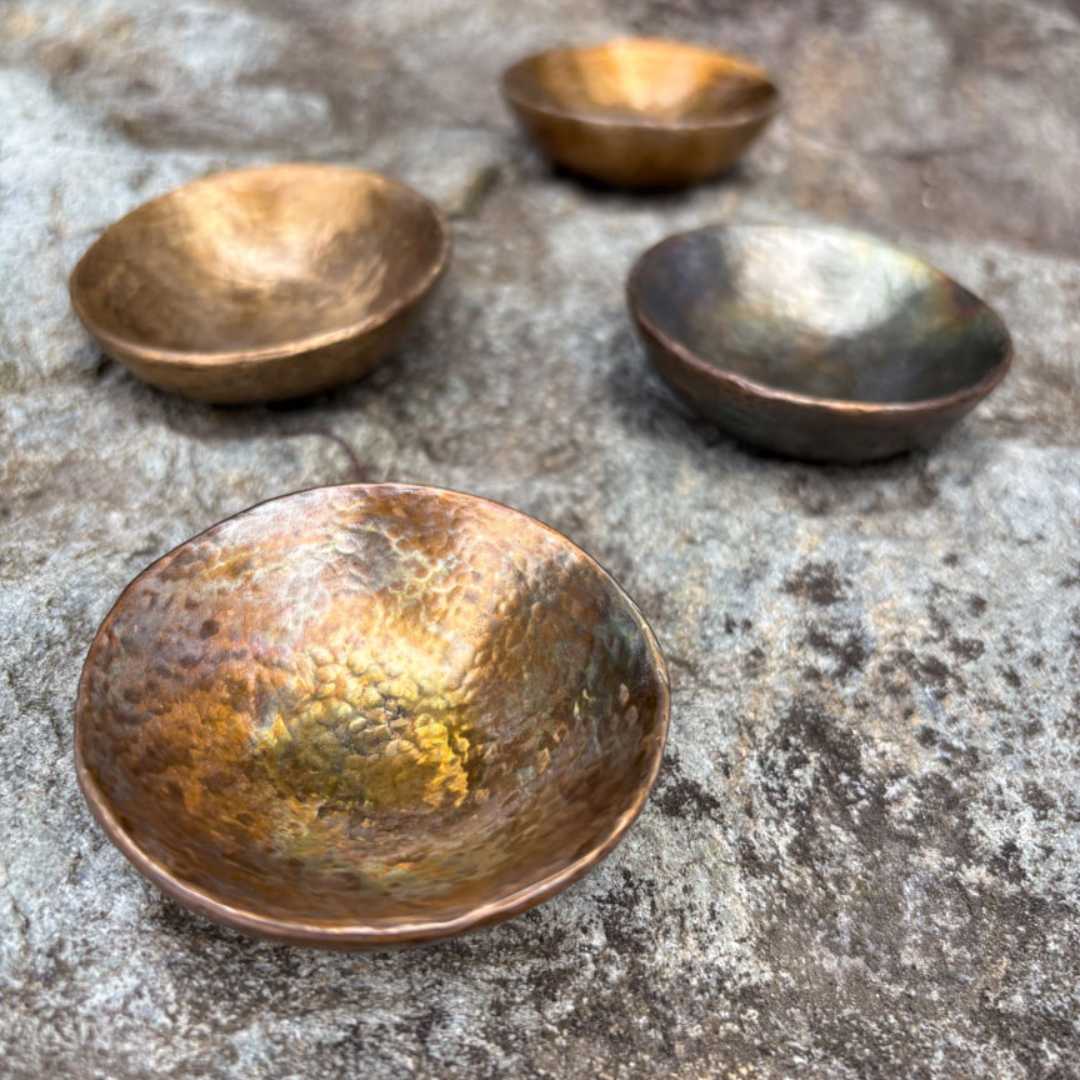 Four handmade cast bronze vide poche catchall bowls showing hammered texture and natural caramel and iridescent patina variations on stone surface, by HerbertandWilks JewelleryJewellery