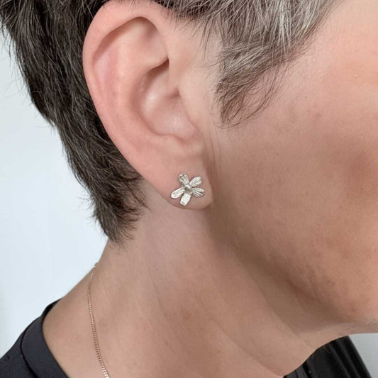 Flora sterling silver flower stud earrings worn on ear showing 12mm scale and sculptural petal detail