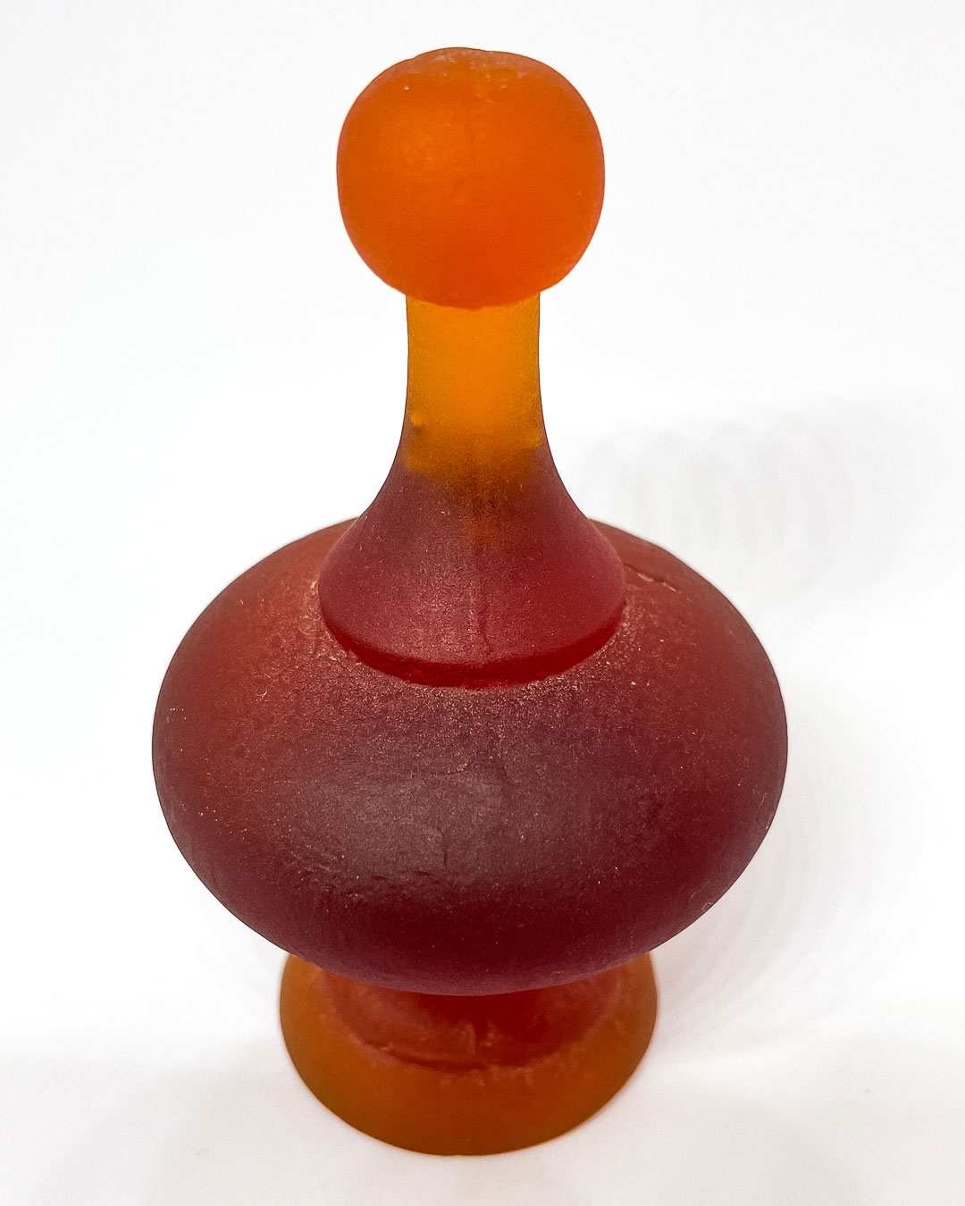 A dark Orange Cast Glass Finial  lit to showcase its intricate curves and varying depths, highlighting the glass's colour tones and translucency.