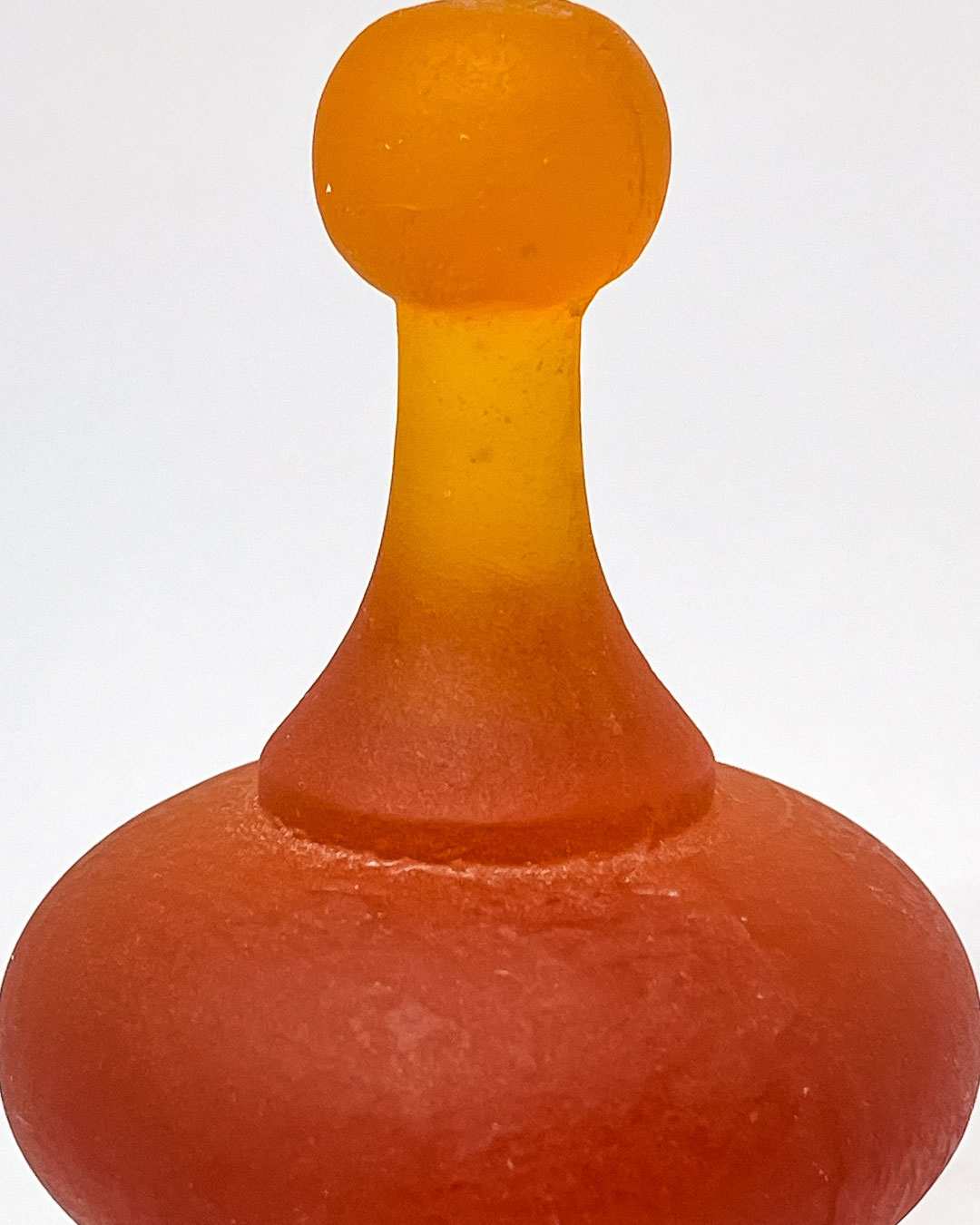 A close up of a Orange Cast Glass Finial  lit to showcase its intricate curves and varying depths, highlighting the glass's colour tones and translucency.