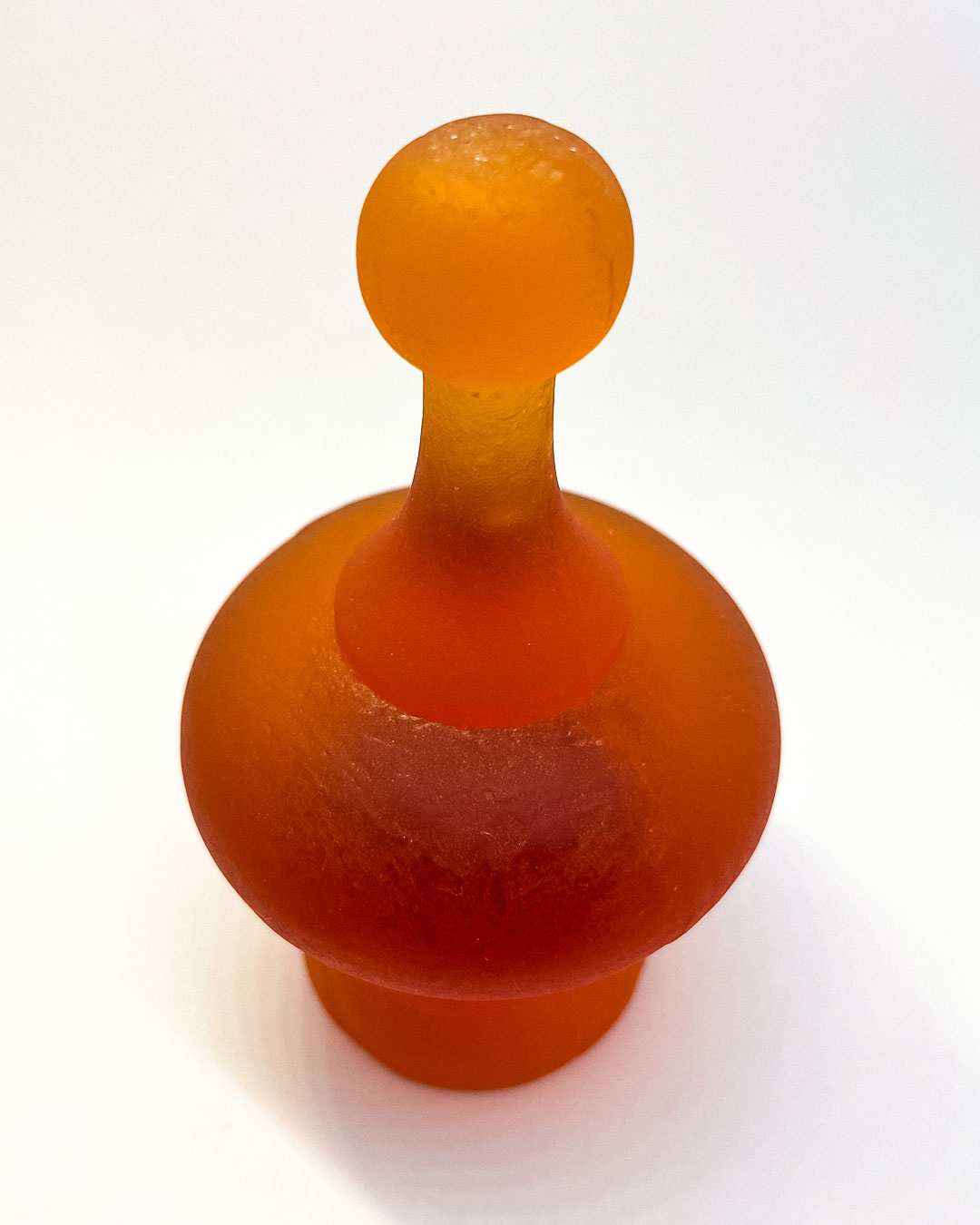 A top down view of the Orange Cast Glass Finial  lit to showcase its intricate curves and varying depths, highlighting the glass's colour tones and translucency.