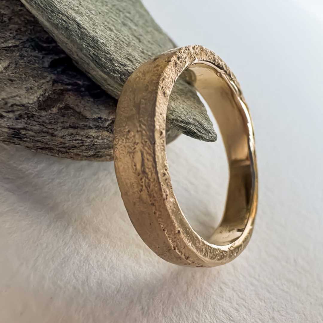 4mm Sandcast Ring – Flat Face in 9ct Yellow Gold leaning against natural rocks, showing both the organic textured outer surface and smooth inner band — HerbertandWilks Jewellery