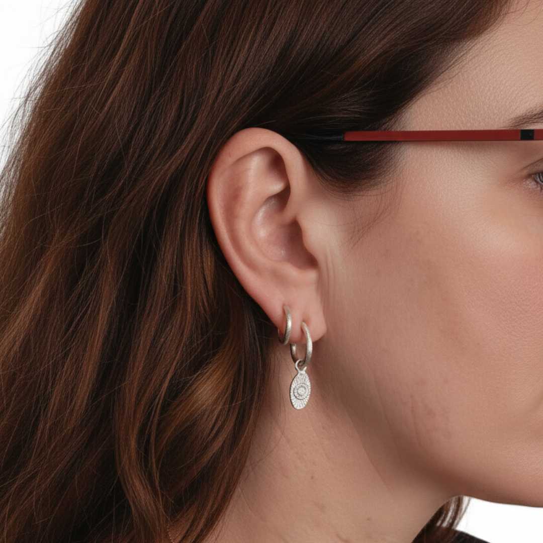 Woman with long auburn hair wearing 13mm and 14mm textured sterling silver hoop earrings with diamond Strata charm on 14mm hoop against white background