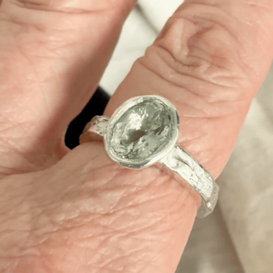 Manatū aquamarine ring worn on the hand, showing the pale blue-green stone and textured sterling silver band in movement.