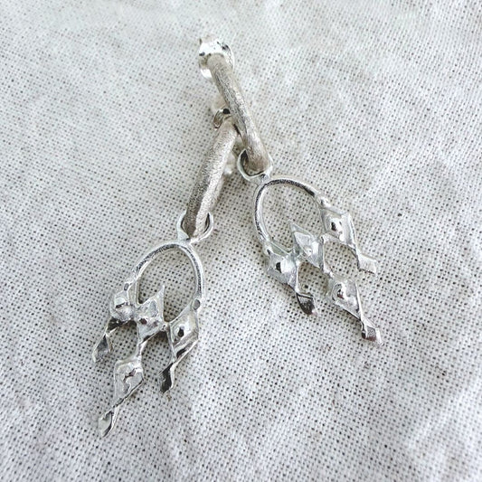 Close-up of sterling silver Arbour earrings on natural linen showing textured hoops and sculptural open details.