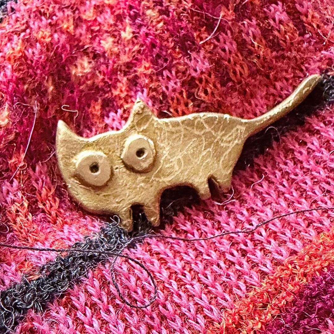 Handmade bronze Cat Pin shown on red and pink woolen fabric