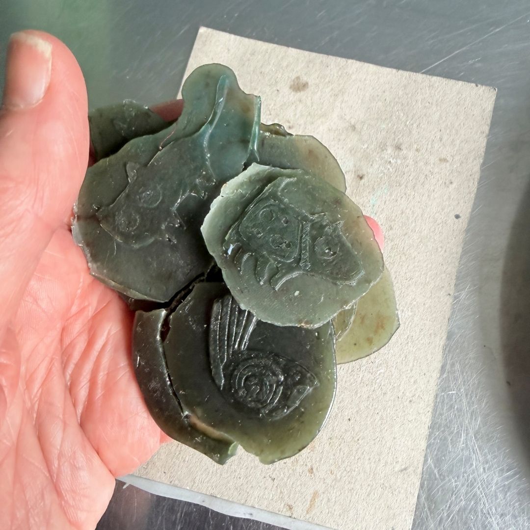 Handmade wax pin designs held in the hand, showing textured collage details ready for cleaning up and casting.