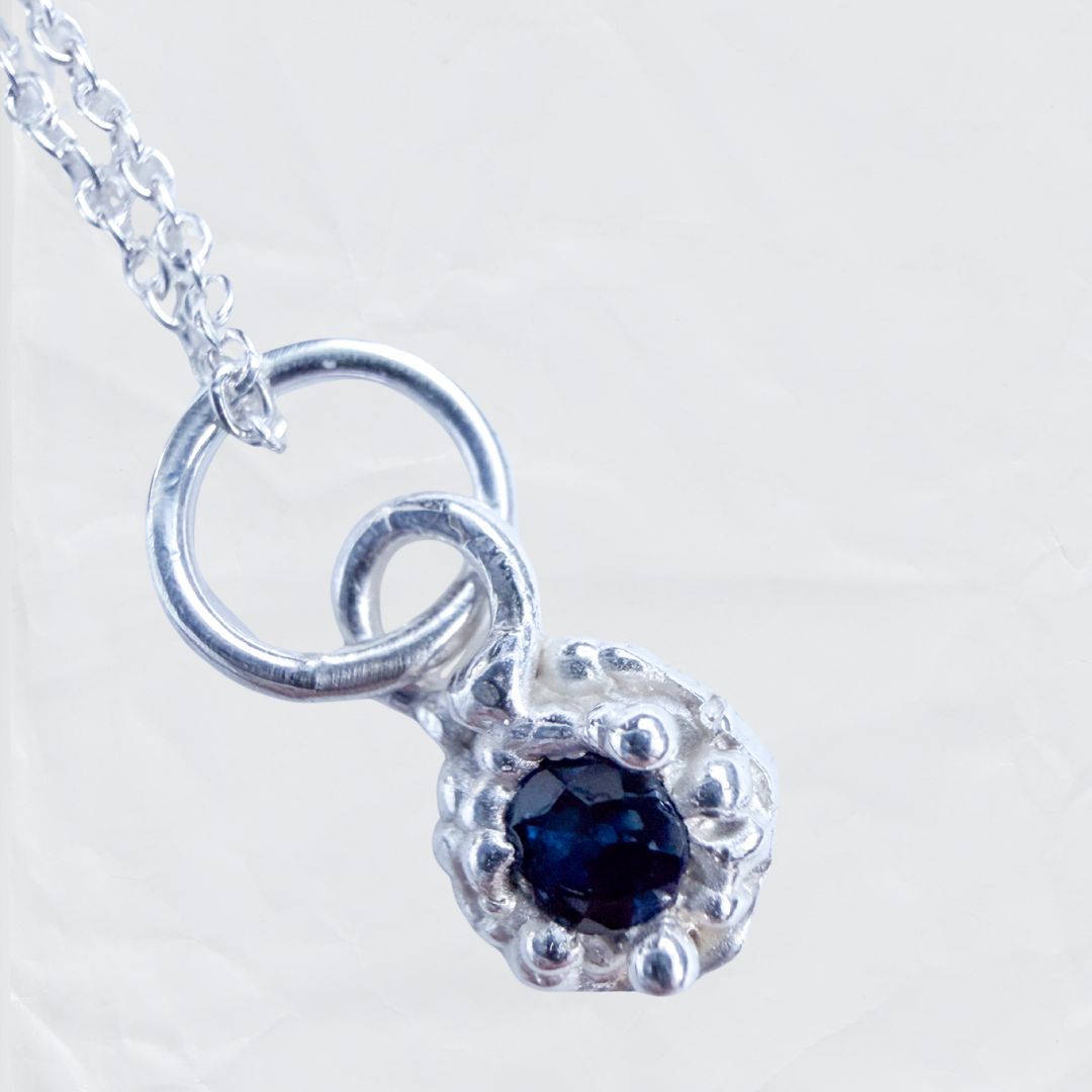 Fluid Dewdrop sterling silver pendant necklace displaying a 3mm natural blue sapphire on a fine cable chain, set against a plain neutral background.