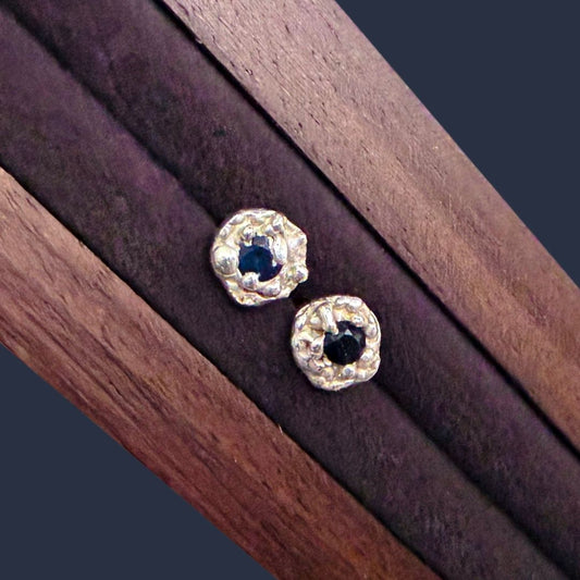 Pair of handcrafted sterling silver Dewdrop Sapphire Stud Earrings with dark blue sapphires and irregular textured silver surrounds.