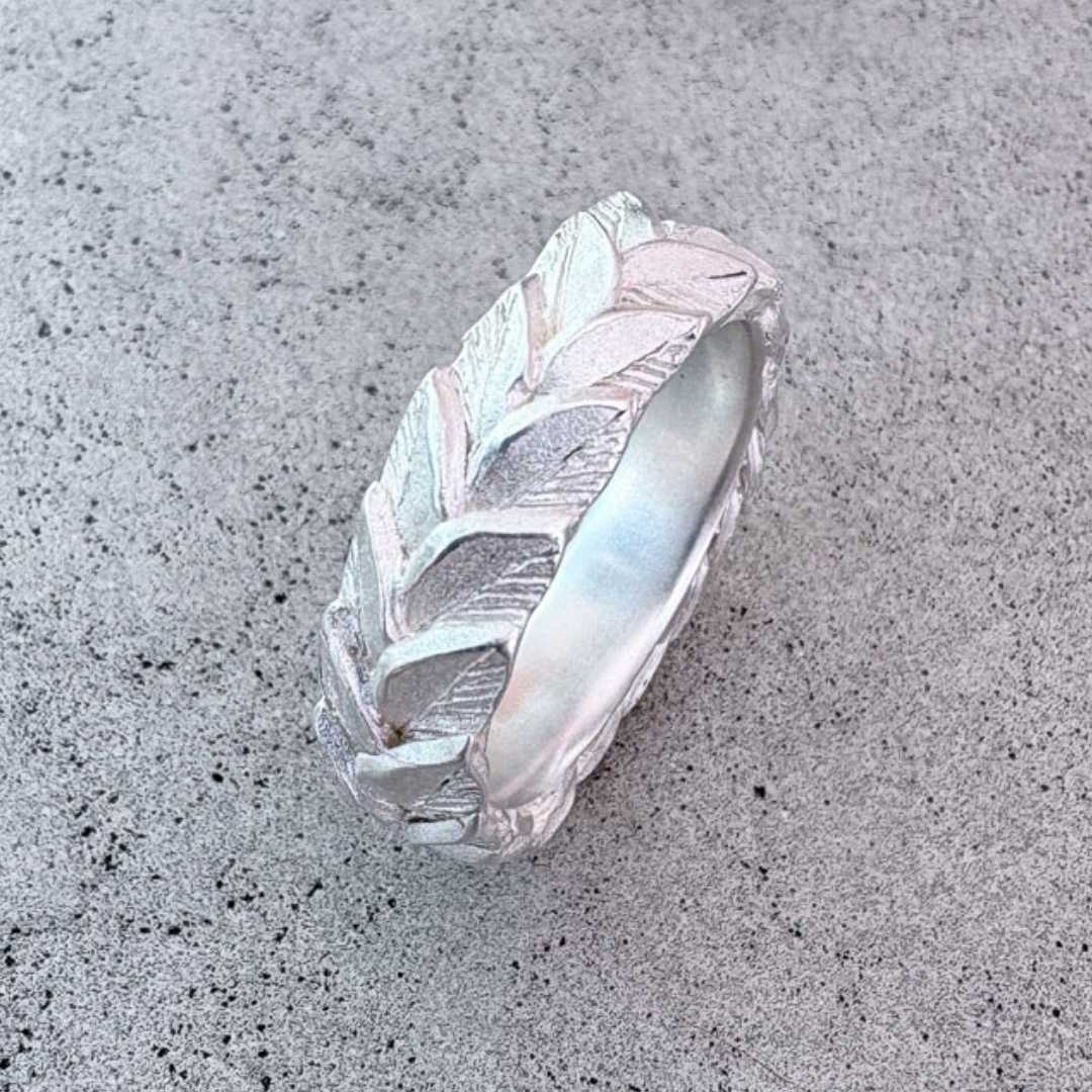 Sterling silver double leaf ring band with satin finish viewed from front angle on concrete surface, showing three-dimensional laurel leaf texture