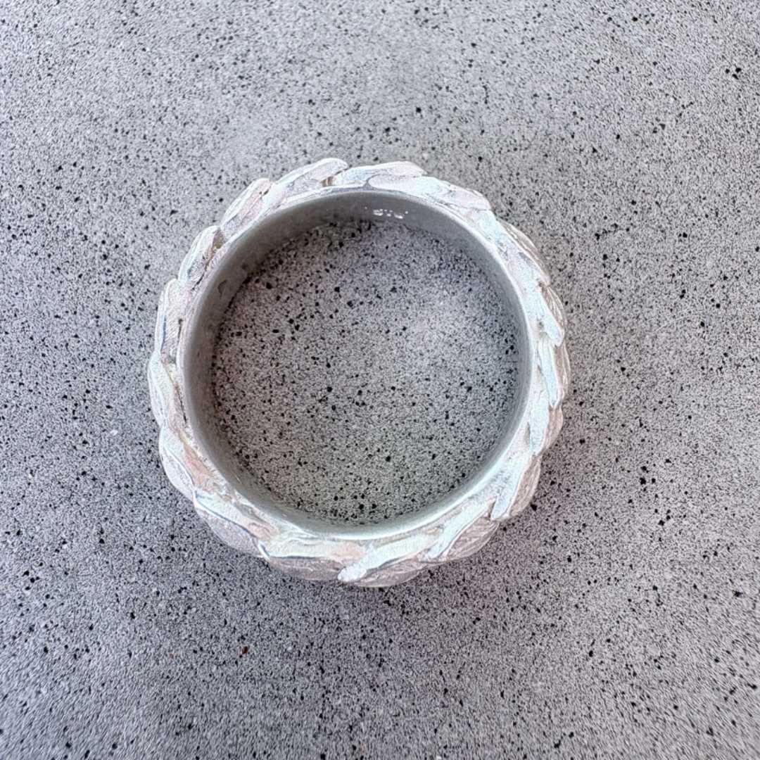 Overhead view of hand-carved laurel leaf wedding ring in sterling silver on concrete background, showing sculptural overlapping leaf construction