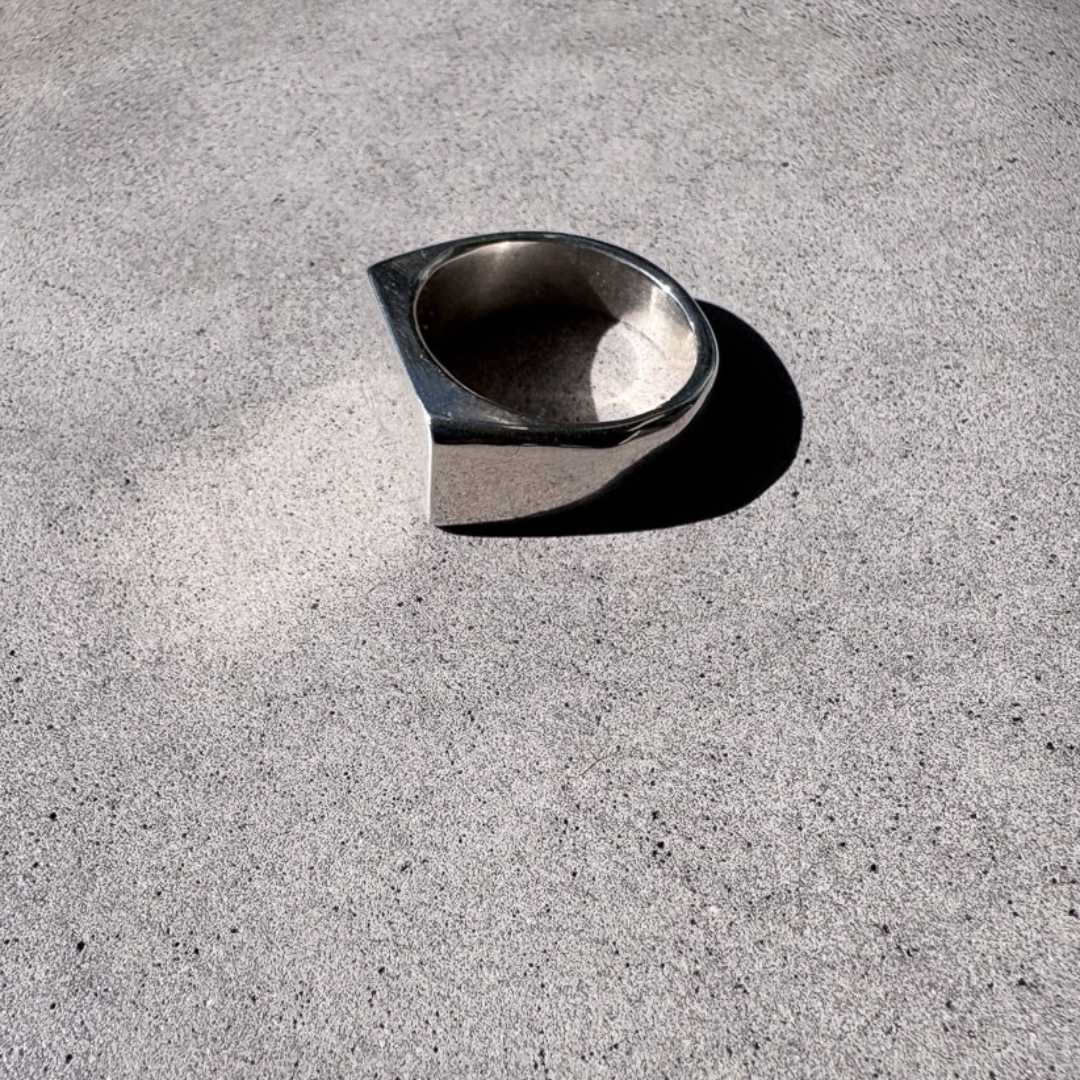 Eden Signet Ring side view from above, showing smooth polished face reflecting light onto concrete surface