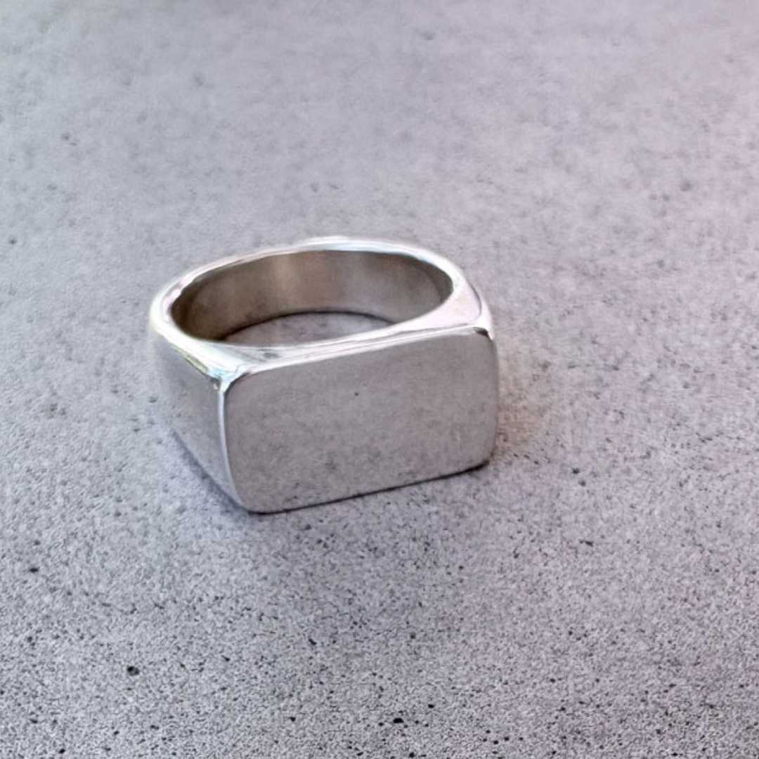 Eden Signet Ring in sterling silver with smooth rectangular face, angled view showing polished reflection on concrete surface
