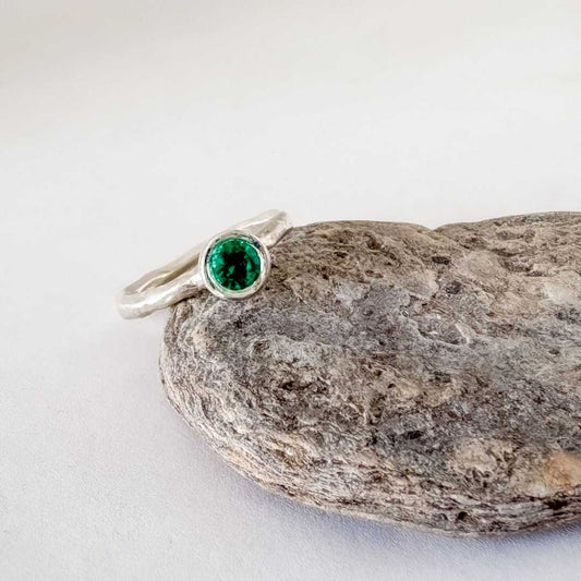 Cherish Ring in sterling silver, Size O, with 5mm Biron emerald leaning against a textured rock.