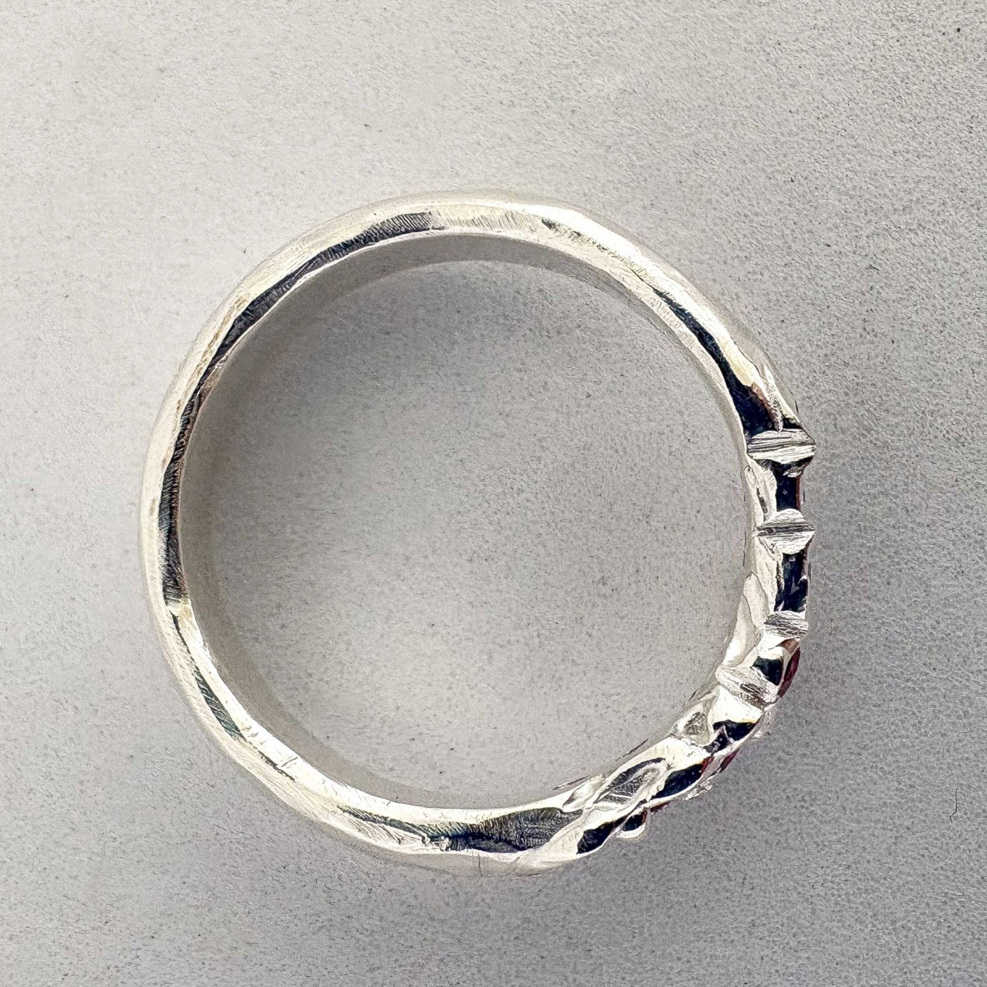 Showing the hand worked surface of the Arc Ruby Ring in sterling Silver from the top view against a light grey background