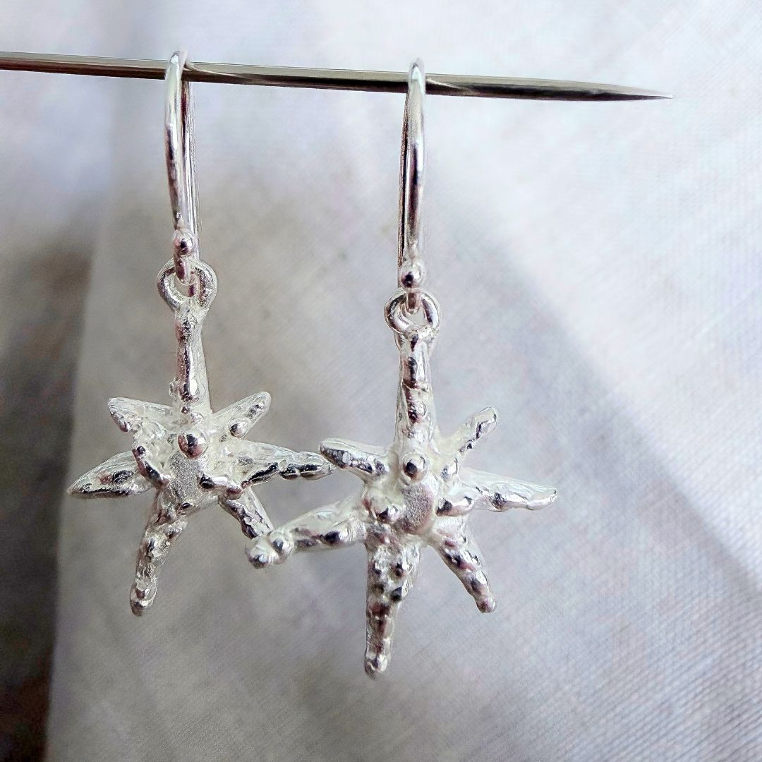Close-up of sterling silver Faerie Star dangle earrings hanging from a pin, showing their irregular sculptural texture and movement.
