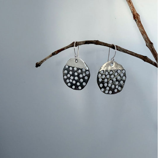 Sculptural sterling silver Filtered Light earrings hanging from a branch, with hand-pierced openings and oxidised detail.