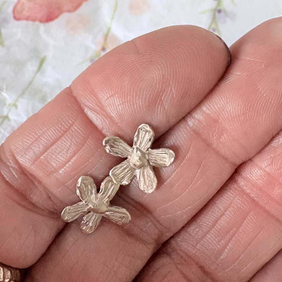 Flora Stud Earrings - 9ct yellow gold flower studs held between fingers showing 12mm size and scale