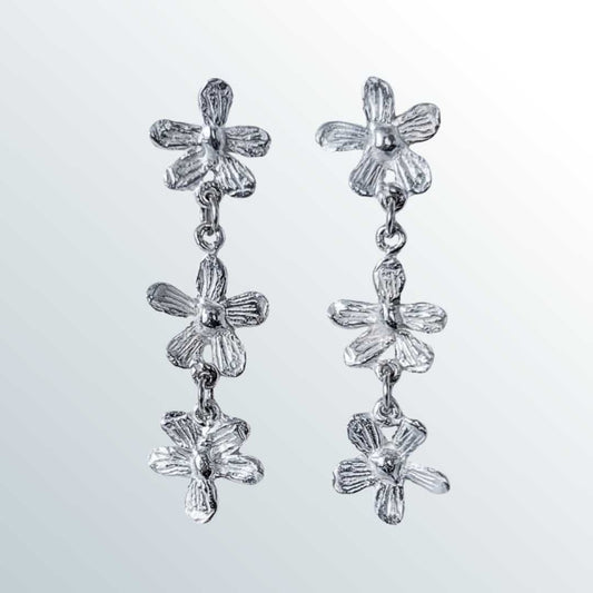 Flora Trailing Flower Earrings 45mm sterling silver botanical drop earrings ona graduated smokey blue-white background showing three hand-sculpted flowers with organic texture and cascading design - handmade in Auckland New Zealand