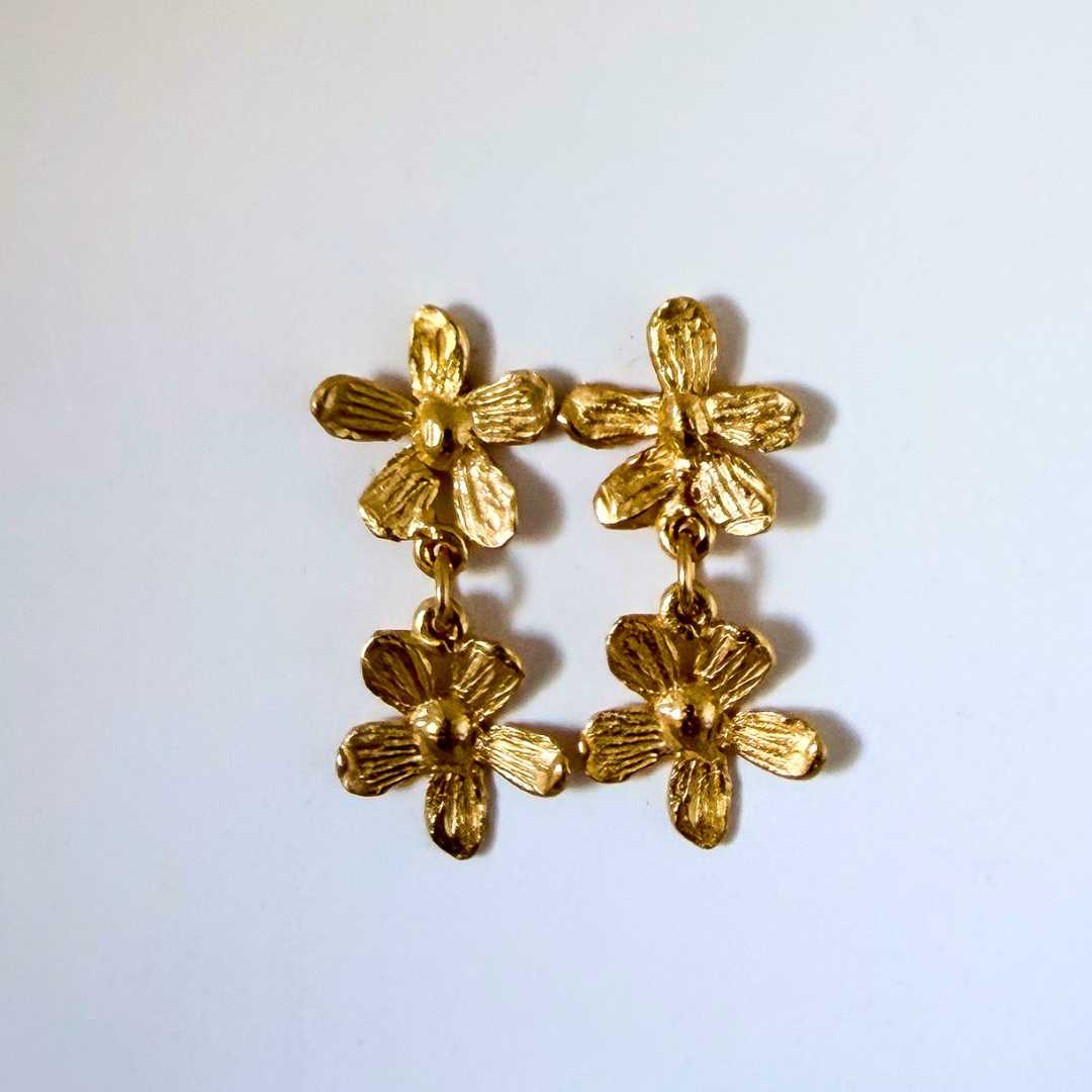 Flora Duo Drop Stud Earrings in 18ct gold plate against a soft blue background, showing the warm gold finish and two-flower botanical form. Handmade in Auckland, New Zealand.