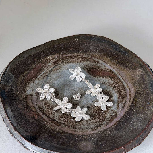 Flora Trailing Flower Earrings resting on handmade ceramic plate with one butterfly back removed - sterling silver botanical earrings displayed on artisan pottery - New Zealand made jewellery