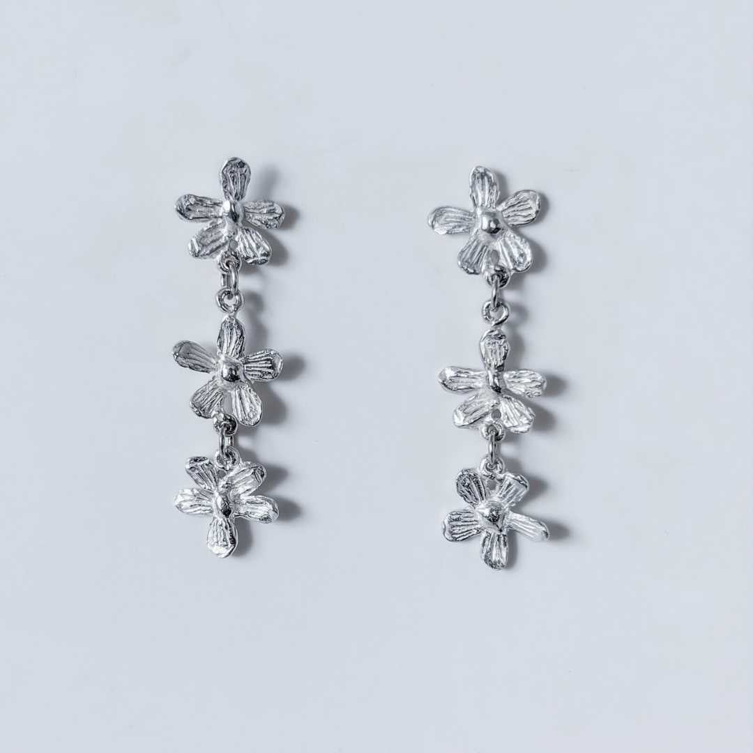 Flora Trailing Flower Earrings 45mm sterling silver botanical drop earrings on light blue-grey background showing three hand-sculpted flowers with organic texture and cascading design - handmade in Auckland New Zealand