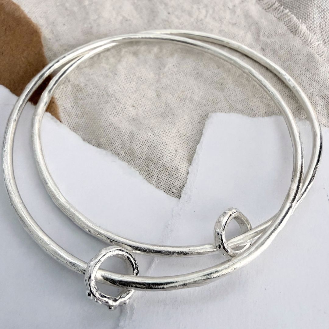 Pair of organic sterling silver bangles with loose Fluid ring details, shown layered together