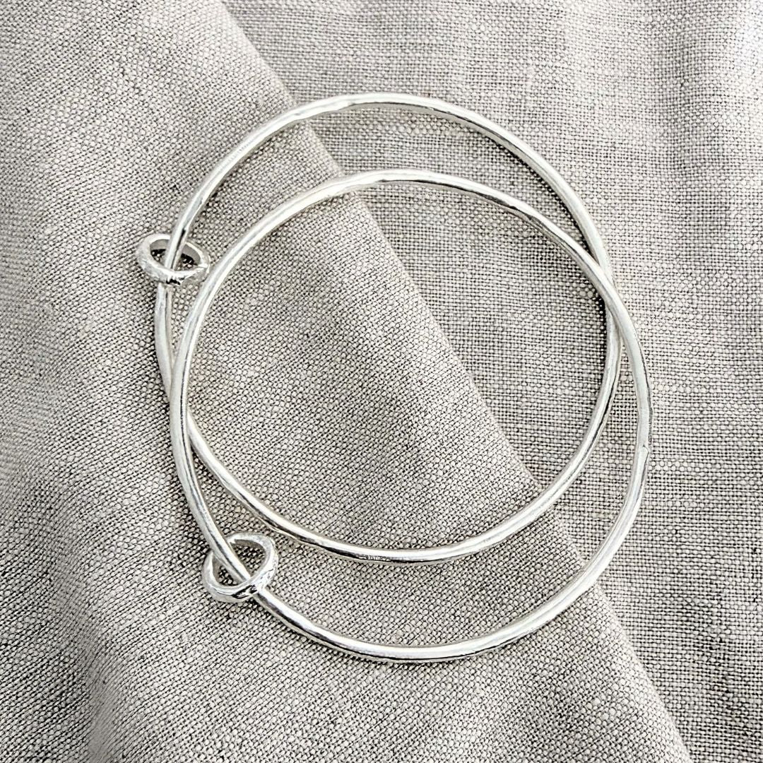 Two sterling silver Fluid Ring Bangles layered together, showing their irregular hand-sculpted surfaces