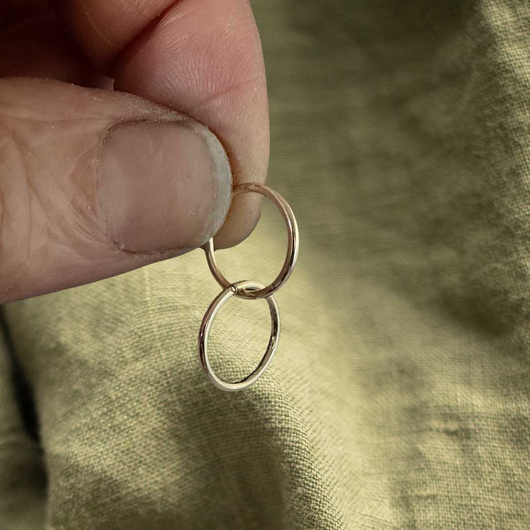 12mm 9ct gold sleeper earrings held between fingers against a textured green linen fabric background, showcasing the delicate scale of these solid gold everyday hoops.