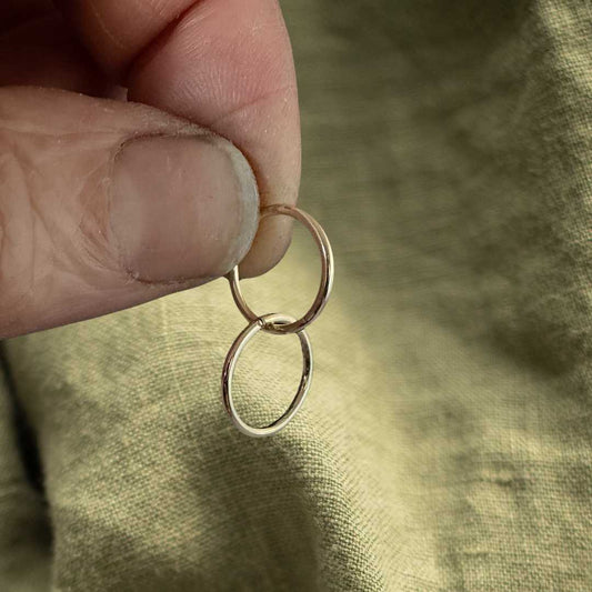 12mm 9ct gold sleeper earrings held between fingers against a textured green linen fabric background, showcasing the delicate scale of these solid gold everyday hoops.