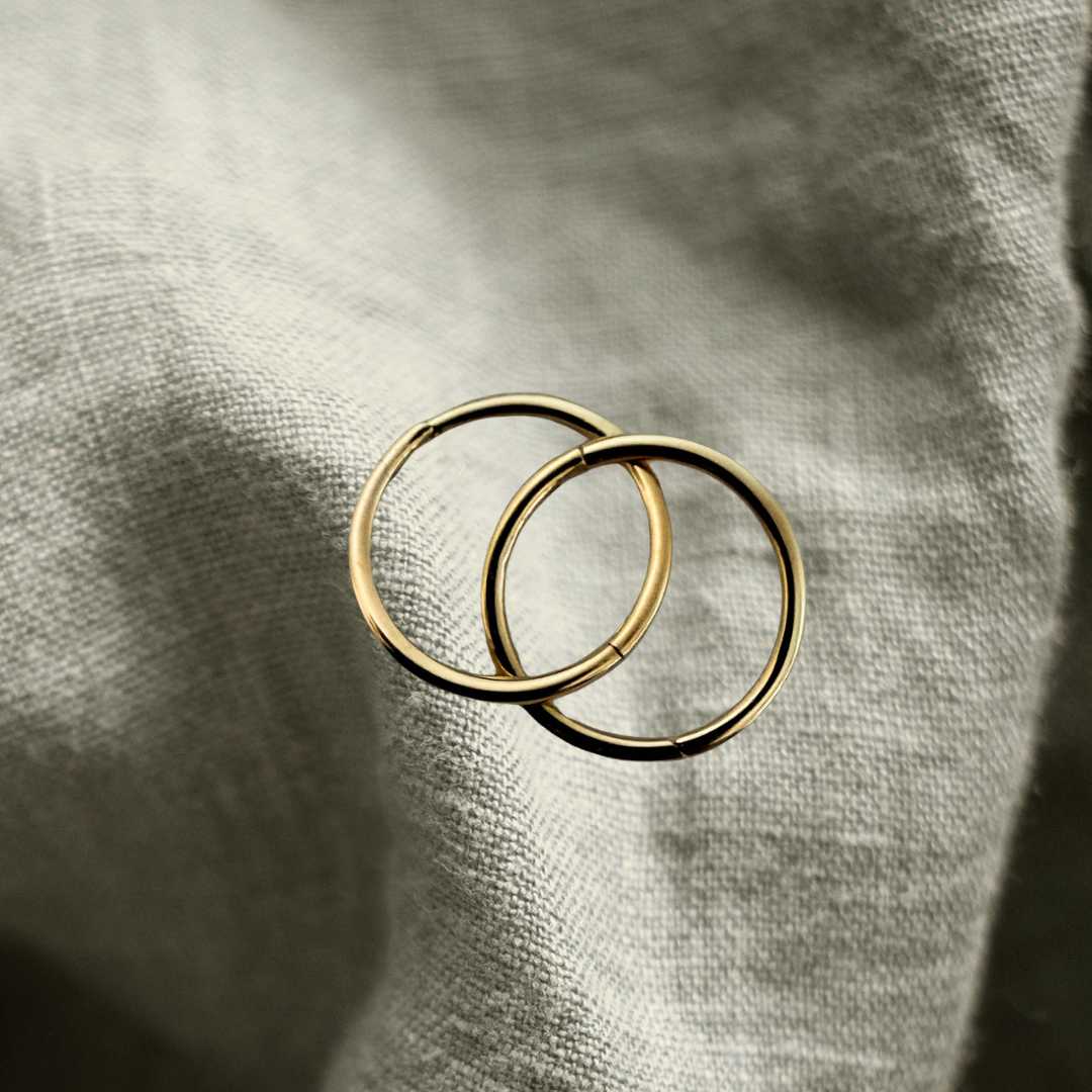 Pair of interlinked 12mm 9ct gold sleeper earrings resting on light textured linen, beautifully showcasing the rich, warm yellow gold color and high-polish finish.