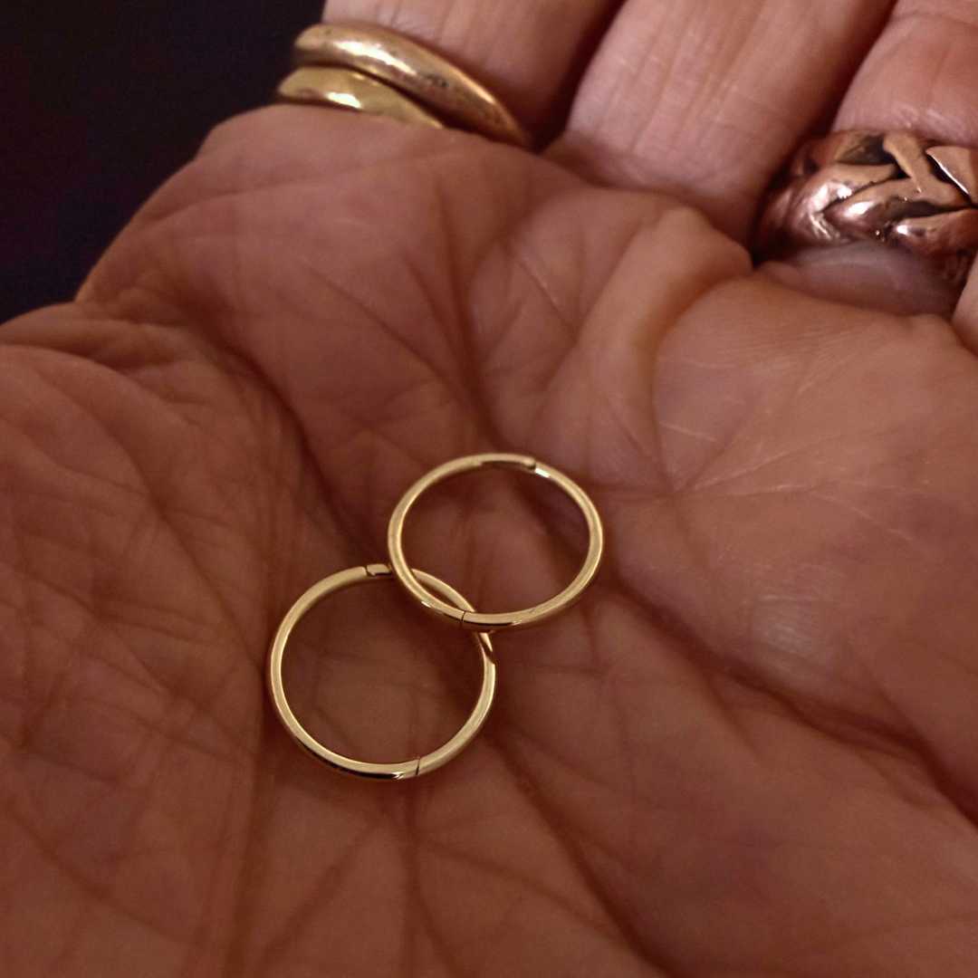 Pair of 12mm 9ct gold sleeper earrings resting in the palm of an open hand, showcasing the delicate scale and warm polished finish of these solid gold hoops.
