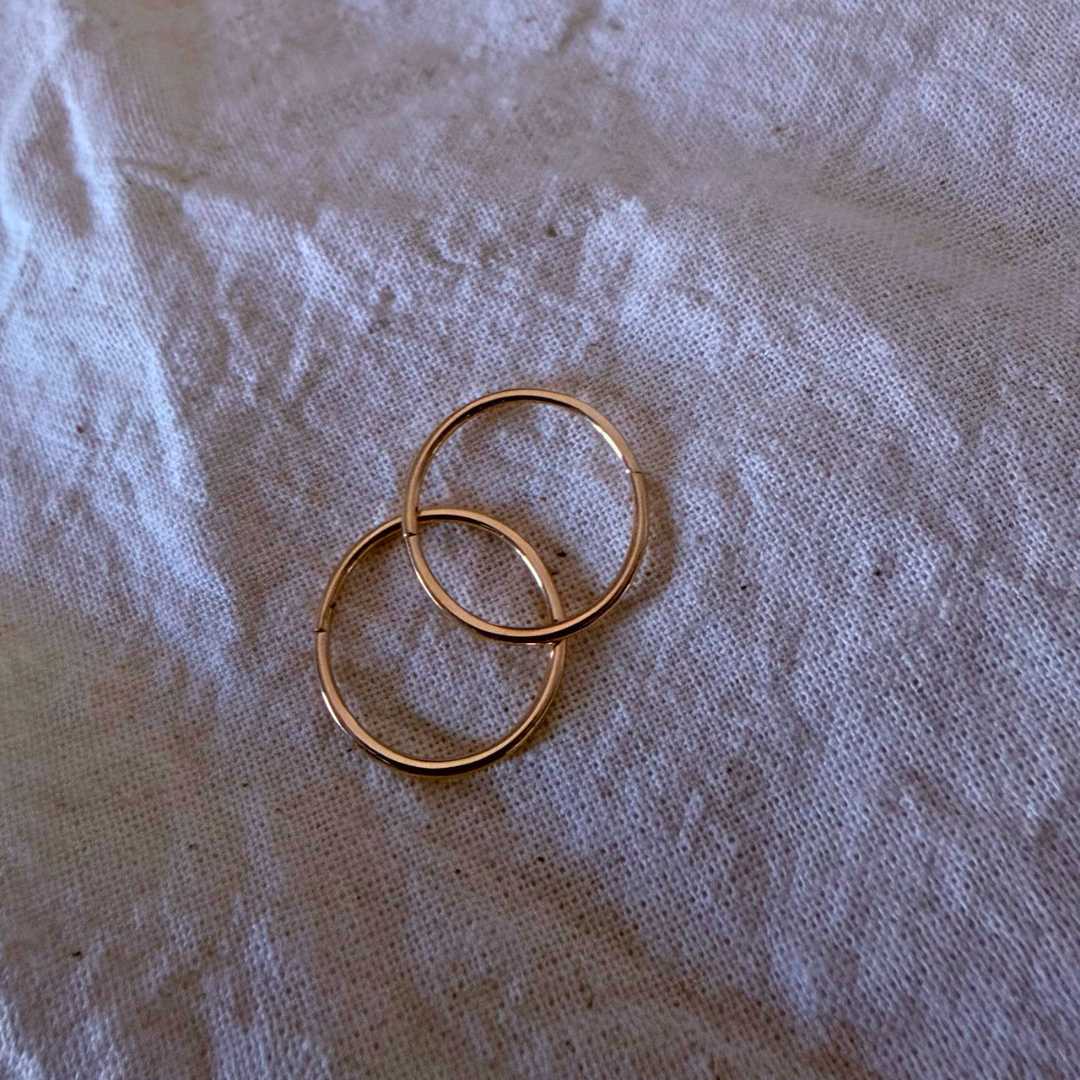 Pair of 16mm 9ct gold sleeper earrings resting on a textured light white linen cloth background, showcasing the slightly bolder standalone scale and rich, warm yellow gold color.