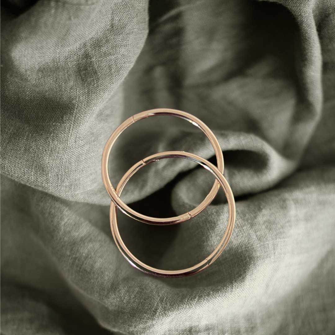 Pair of 16mm 9ct gold sleeper earrings interlinked together on a light green linen cloth background, showcasing the slightly bolder standalone scale and rich, warm yellow gold color.