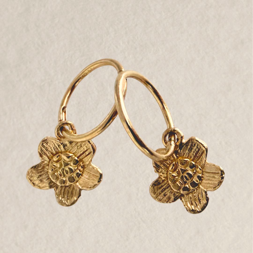 Pair of handcrafted gold daisy sleeper earrings standing side by side on a light neutral surface.