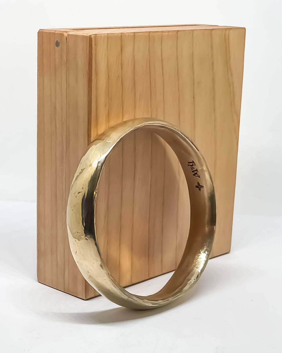 A wide Bronze Bangle showing the makers marks on the inside of the band leaning against a wooden box