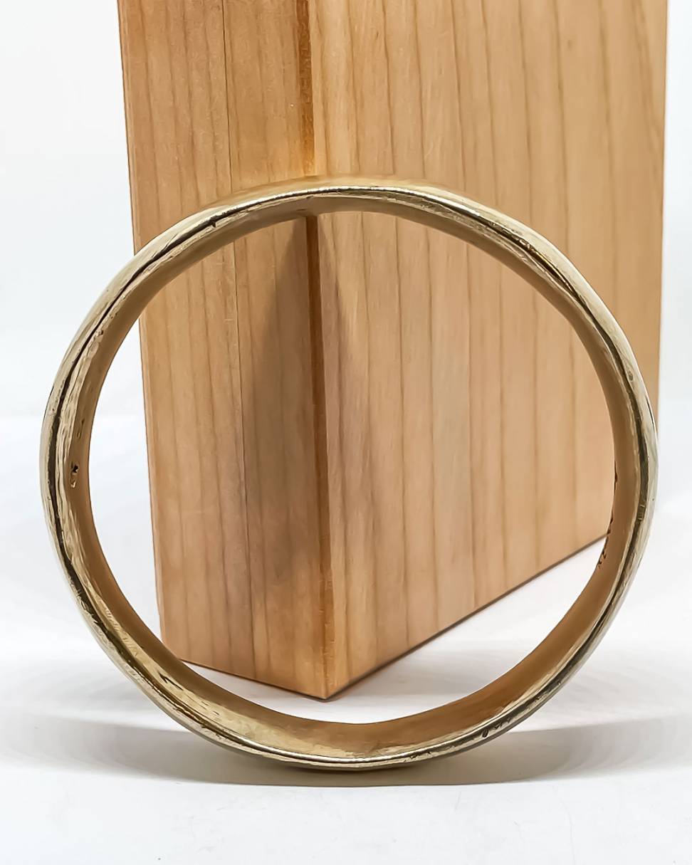 A wide Bronze Bangle showing the thickness of the bangle leaning against a wooden box