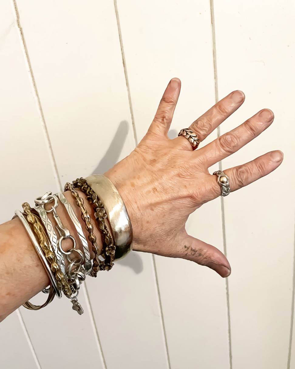 A wide Bronze Bangle shown as part of a stack of bangles and chains on a persons wrist