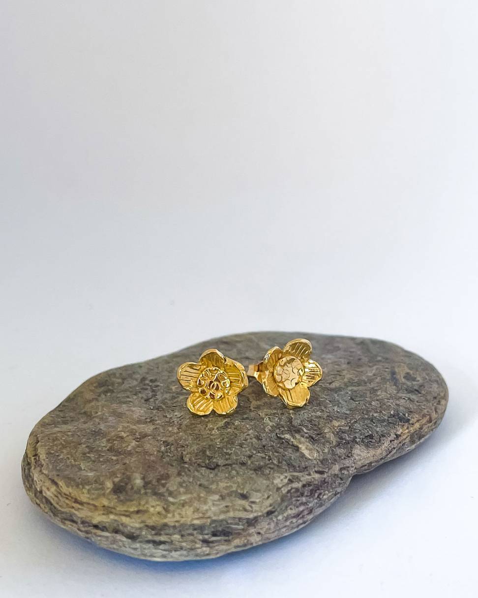 a pair of Golden Daisy Flower Stud Earrings sitting on a rock