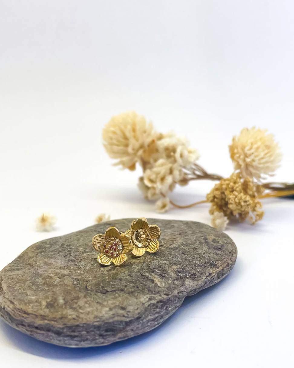 a pair of Golden Daisy Flower Stud Earrings sitting on a rock with flowers behind