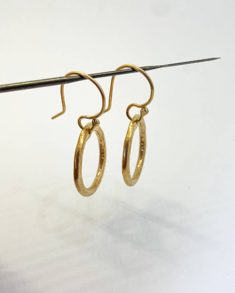 A pair of 18ct Gold plated organic Circle hoop earrings hanging from a needle
