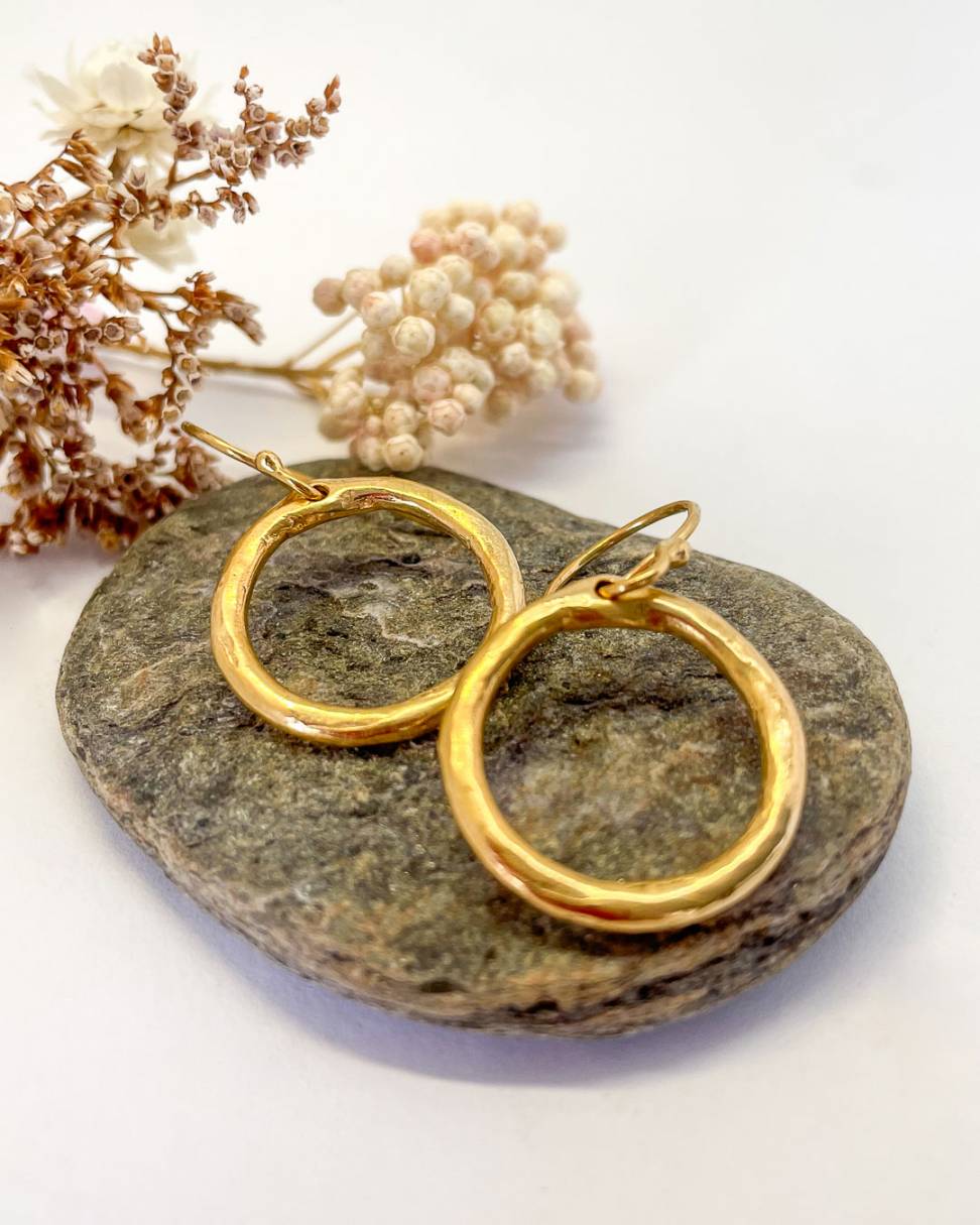 A close up of a pair of Organic Circle 18ct Gold Plated Hoop Earrings sitting on a rock