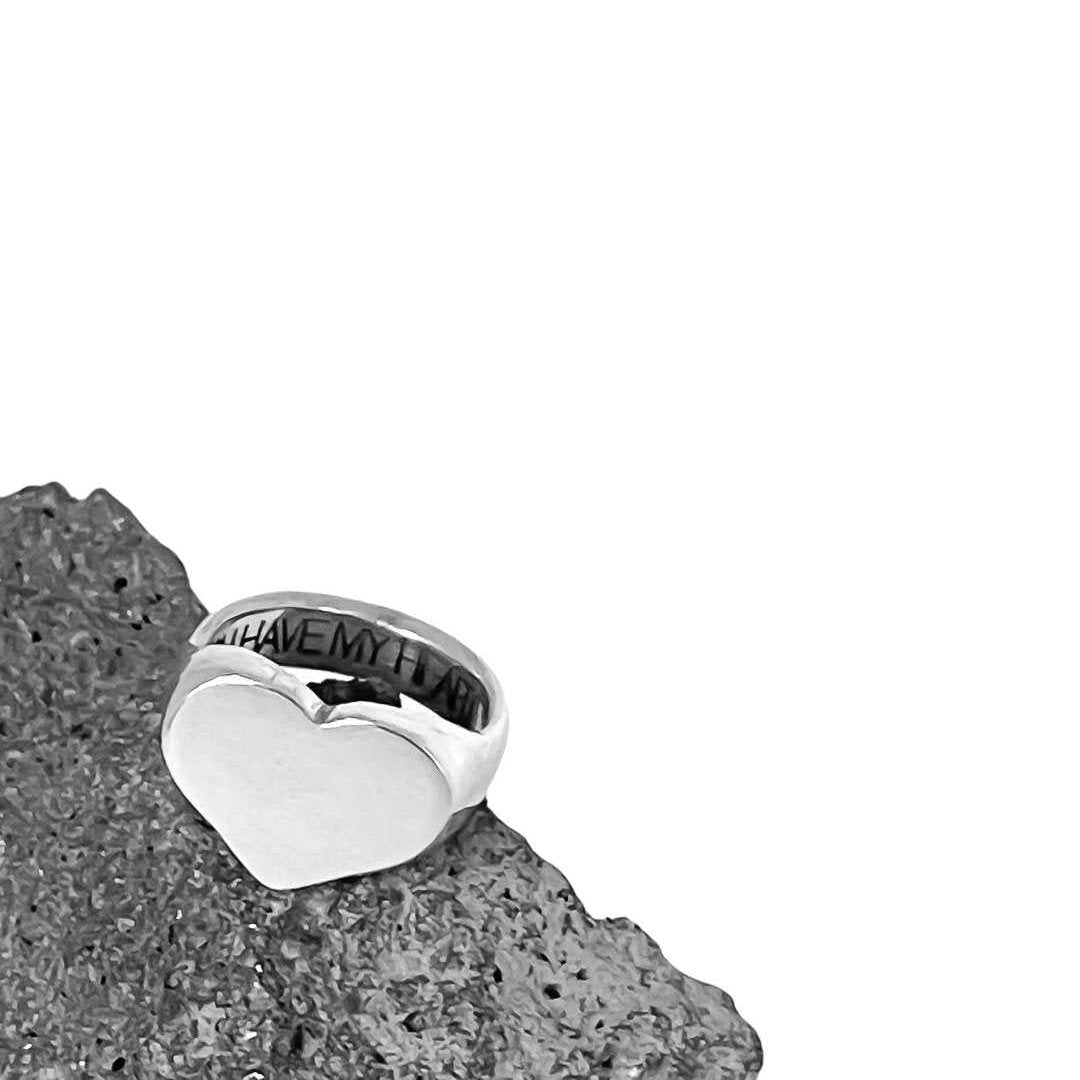 A close up of the Heart Signet Ring in sterling silver sitting on a piece of Volcanic Scoria showing the front face and the engraving on the inside of the ring band .