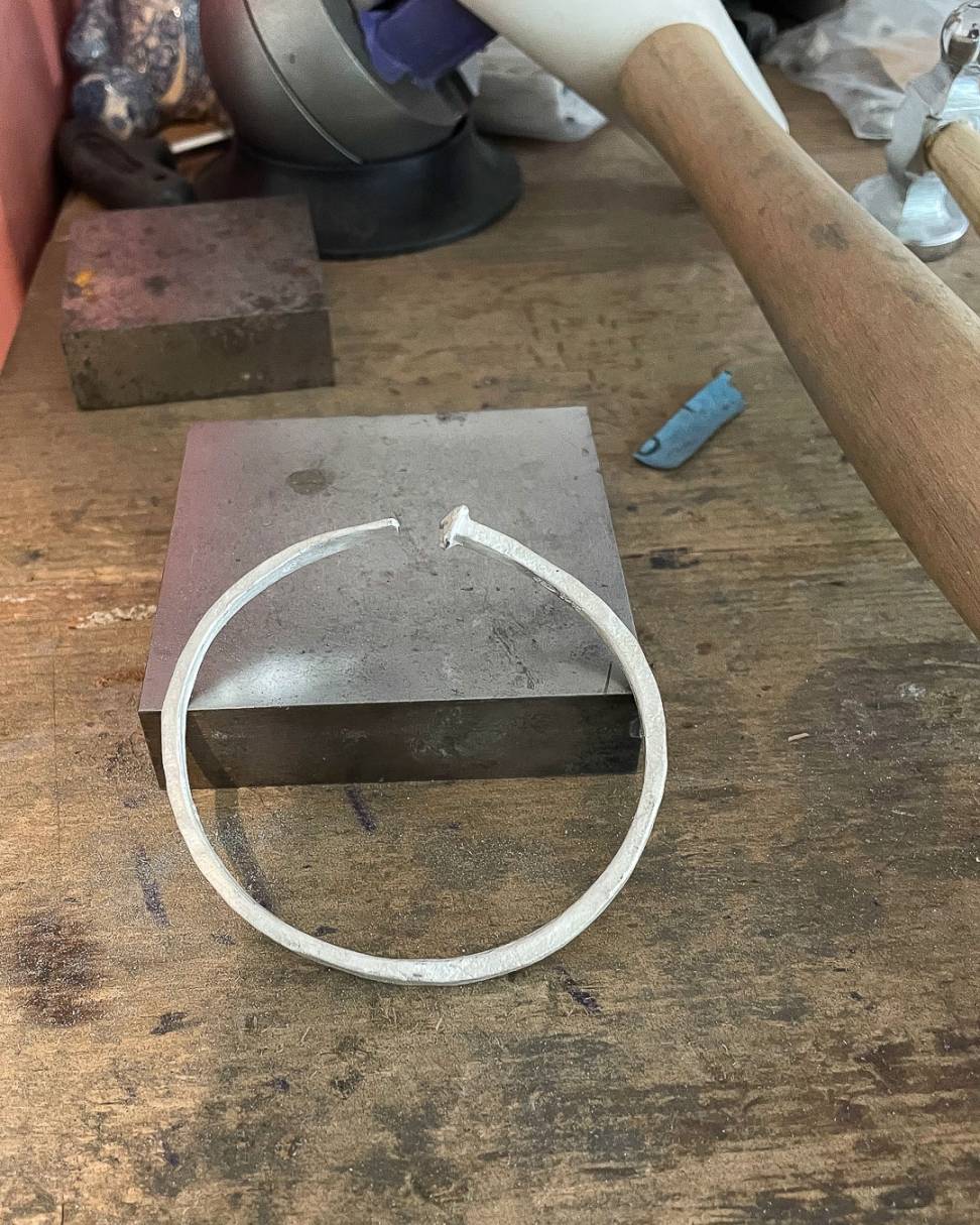 A close up image of the Sterling Silver Sheet Cut Nail Cuff resting against a steel block in the jewellers workshop