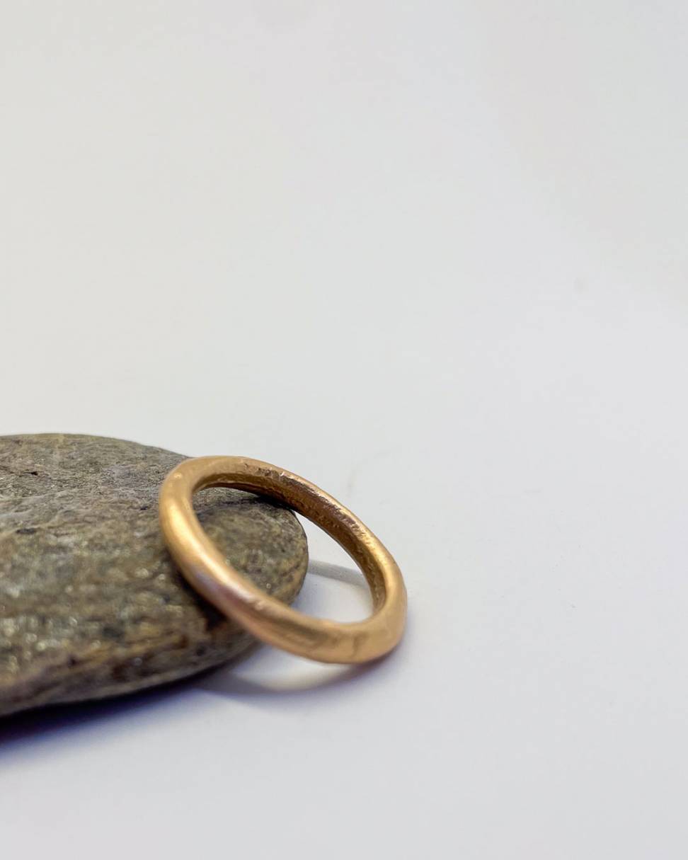 A 3mm 9ct Yellow Gold Sand Cast ring leaning against a stone