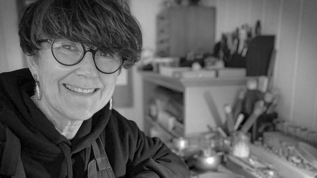 Sally Herbert, jeweller at HerbertandWilks, seated at her workbench in Mt Eden Auckland, looking toward the camera in a black and white studio portrait