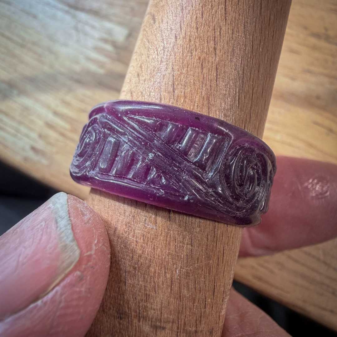 Unfinished hand-carved wax ring on a mandrel at the workbench, showing the raw carved surface before casting