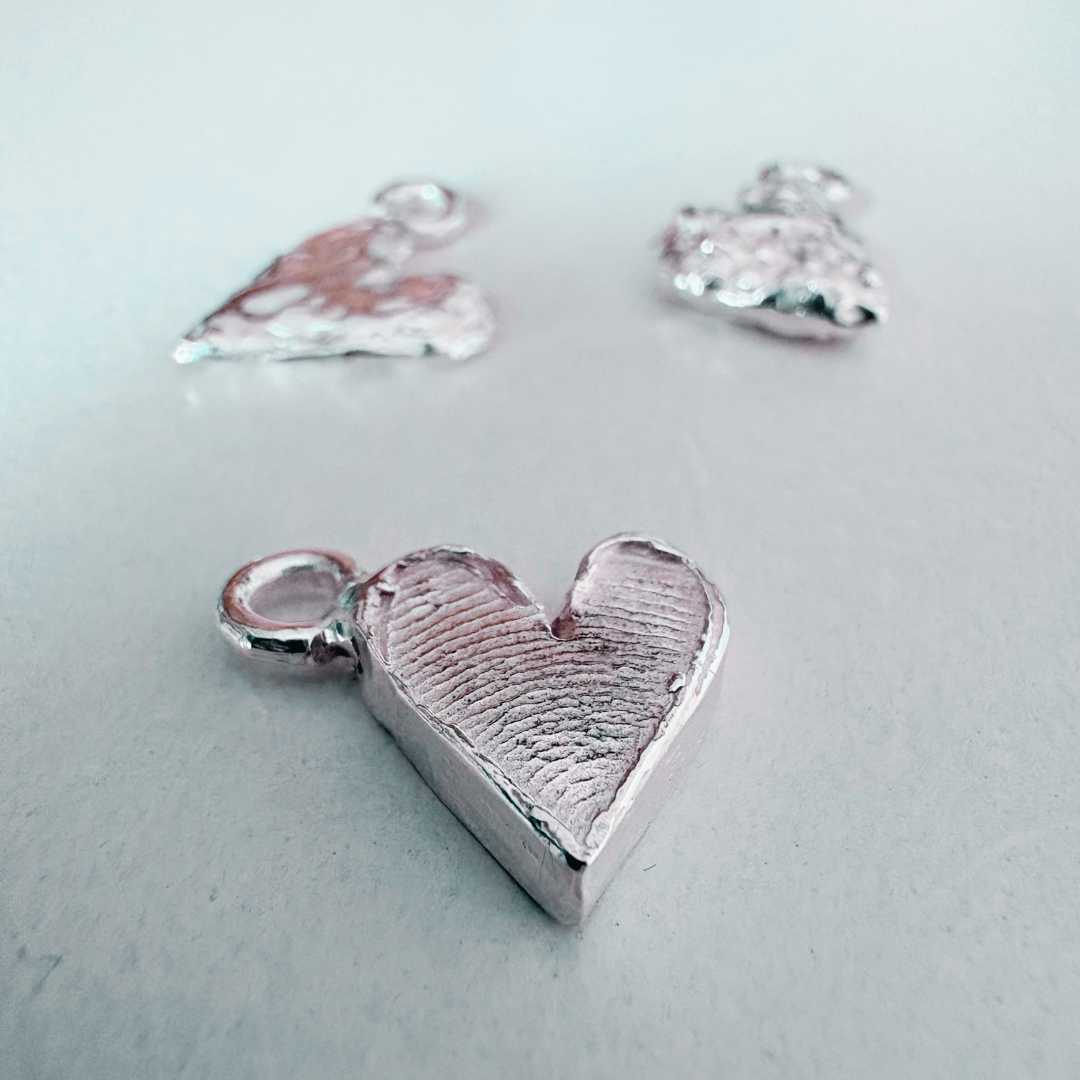 Silver fingerprint heart charm in focus with blurred heart charms in background showing finished workshop results