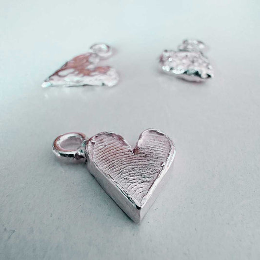 Silver fingerprint heart charm in focus with blurred heart charms in background showing finished workshop results