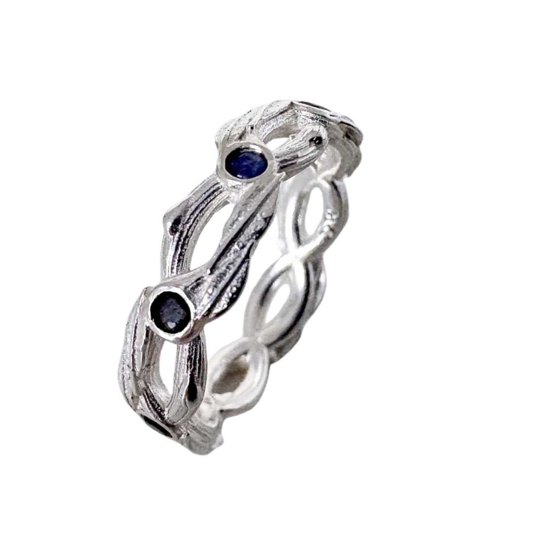 Interwoven pōhutukawa sapphire ring in sterling silver, front-on view tilted to show delicate band interior and eight blue sapphires on white background